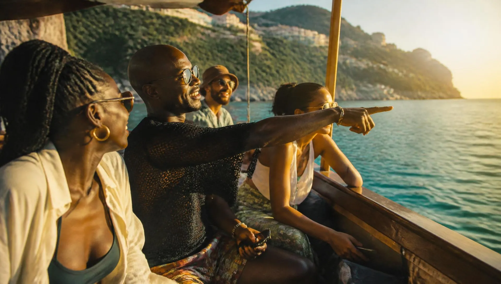 Friends laughing and pointing at the coastline from a small wooden boat on turquoise water at golden hour